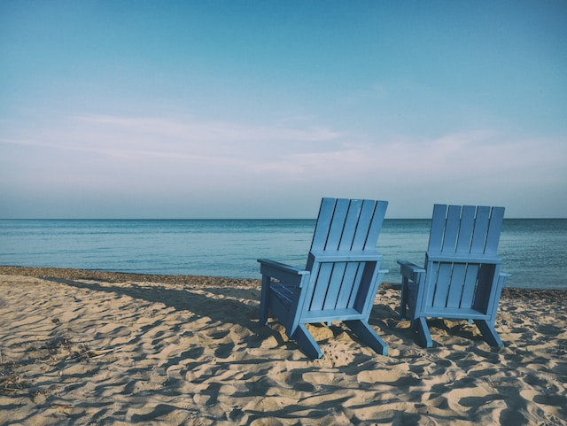 two blue chairs on a beach looking at the ocean