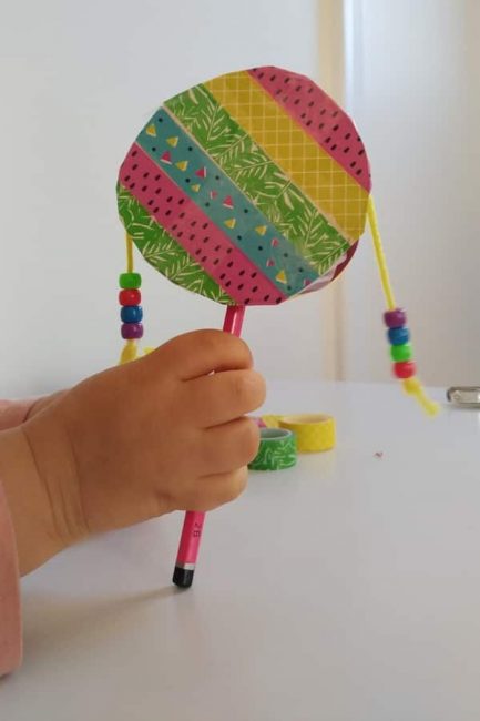 child's hand holding a homemade spin drum with beads
