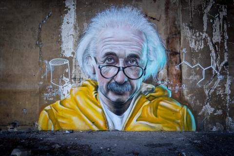 spray painted picture of einstein with a yellow jacket on brick wall