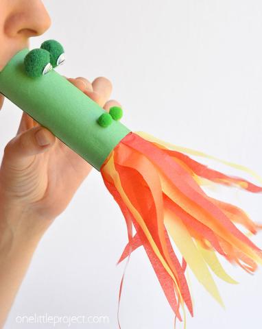 hand and mouth blowing a green tube with orange and yellow streamers