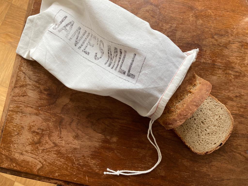 loaf of bread with a white bag on a wooden breadboard